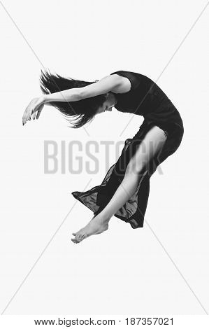 Beautiful modern dancer young woman in black flyings fabrics making dance moves. Isolated on white background. Copy space. Monochrome.