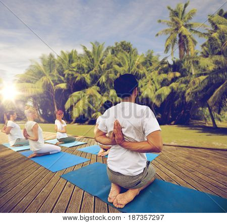 fitness, sport, yoga and healthy lifestyle concept - group of people exercising in reverse prayer pose over natural background with palm trees 