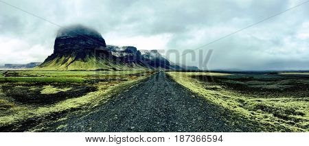 Barren black volcanic road cutting through green moss covered lava fields in Southern Iceland