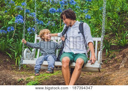 Father And Son Having Fun On Swings In A Flower Garden