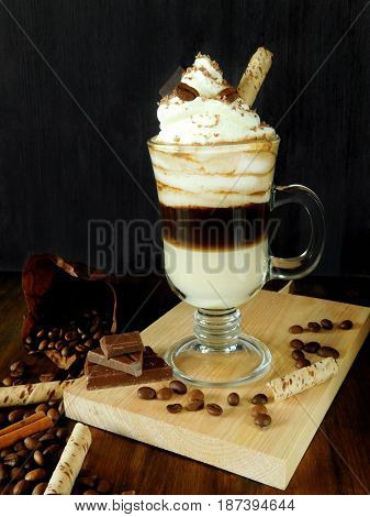 Coffee cocktail with whipped cream in an Irish coffee mug surrounded by coffee beans, cinnamon and chocolate bars