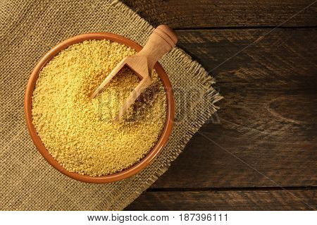 A bowl of raw couscous with a scoop, shot from above on dark rustic textures with a place for text