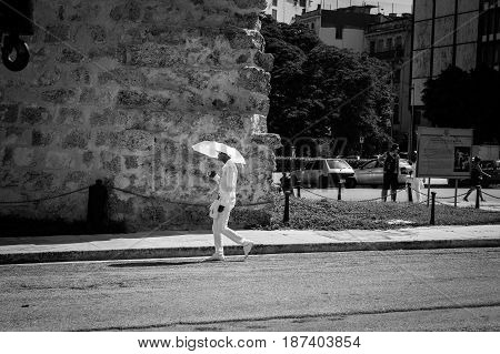 Havana, Cuba - June 30, 2012; member of Santeria Cuban religious sect dressed in all white with umbrella contrasts with rough surrounds as he walks along city street past old stone building Havana.