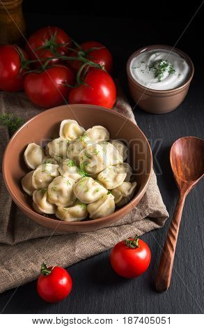 Meat dumplings tomatoes and sour cream on black stonebackground