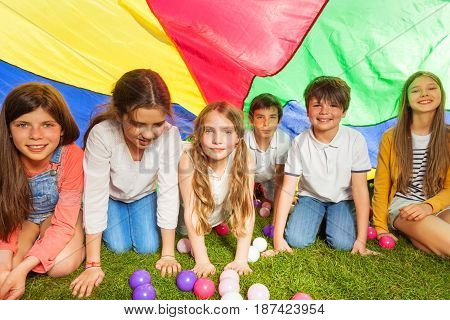 Portrait of happy kids hiding under canopy made of colorful parachute outdoors in summer