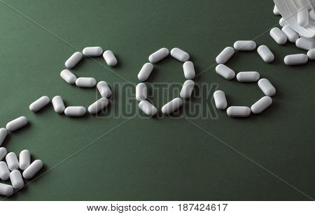 White pills on green background, which forming the word - SOS, with a blister of pills on background. Pharmaceutical or addiction narcotic or depressive or painkiller concept.