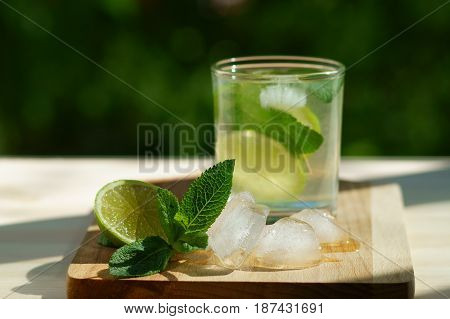 A glass of lime water on a wooden board with ice and mint