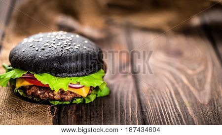 Close up of Homemade Black Burger with Cheese. Cheeseburger with black bun on dark wooden background. Junk food.