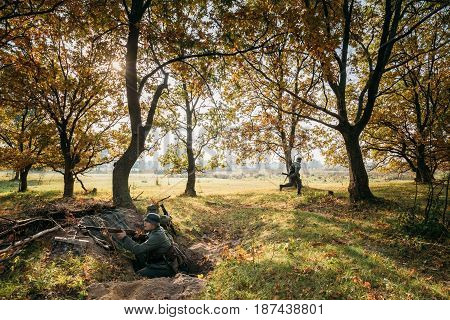 Dyatlovichi, Belarus - October 2, 2016: Re-enactors Dressed As German Wehrmacht Infantry Soldier In World War II Hidden Sitting With Rifle Weapon In An Ambush In Trench In Autumn Forest At Sunrise