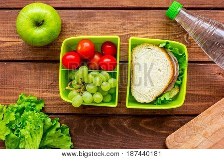 healthy break with apple, grape and sandwich in green lunchbox on home wooden table background flat lay
