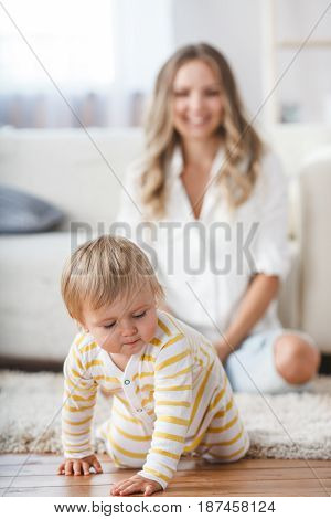 crawling baby boy on living room floor, mothe on second pland out of focus