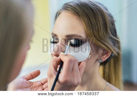 Make-up artist doing smoky eyes makeup to beautiful young girl in the studio Dressing room. The makeup artist tints the eyebrows.