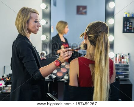 Make-up artist doing smoky eyes makeup to beautiful young girl in the studio Dressing room. The makeup artist tints the eyebrows.