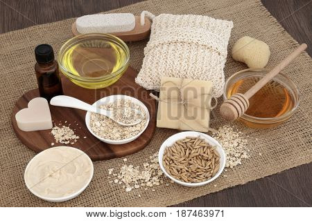 Natural ingredients to heal skin disorders with oats, honey, almond oil, moisturizer, soap and essential oil on hessian over oak wood background. Treatment will help soothe psoriasis and eczema.