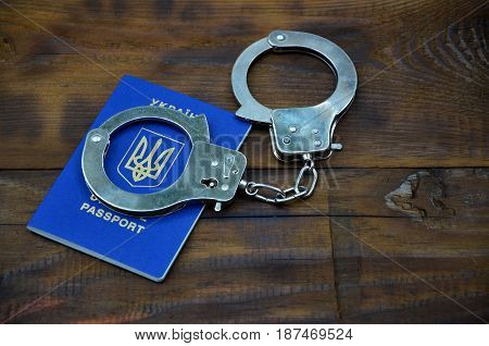 Ukrainian Passport With Police Handcuffs Lies On A Wooden Table. The Concept Of Crime Of Ukrainian C