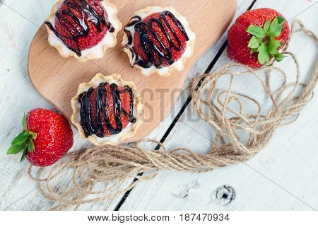 Strawberry cake with vanilla cream on white rusric wooden background. Sweet basket tartlet with strawberries and chocolate. Tasty summer dessert. Top view.