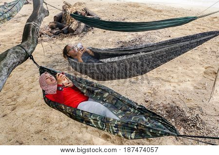 Labuan,Malaysia-Feb 19,2017:Young people playing smartphones while enjoying the hammock on tropical beach in Papan island,Labuan,Malaysia.