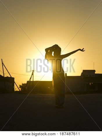 silhouette of girl against the yellow sun rays at sunset with buildings on gackground