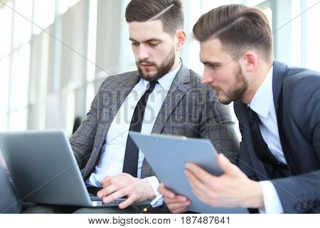 Mature businessman using a digital tablet to discuss information with a younger colleague in a modern business lounge