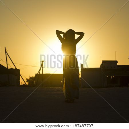 silhouette of girl against the yellow sun rays at sunset with buildings on gackground