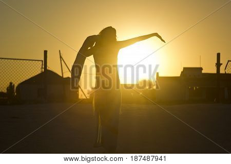 silhouette of girl against the yellow sun rays at sunset with buildings on gackground
