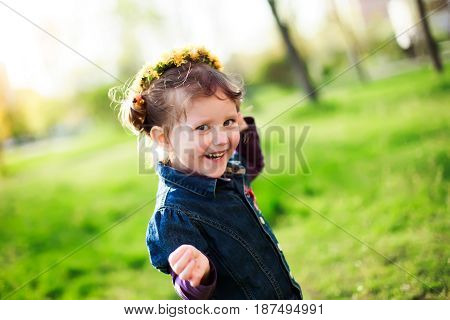 The little girl laughs. Girl running on green grass in the spring. The child on the head with a wreath of yellow flowers dandelions. Free space.