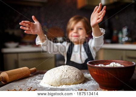 Cute little girl claping hands with flour of a dough in the kitchen. Horizontal indoors shot.