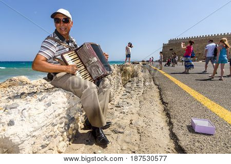 HERAKLION GREECE - JULY 16 2016: Crete. Musician on the waterfront plays accordion. In the background Venetian fortress.