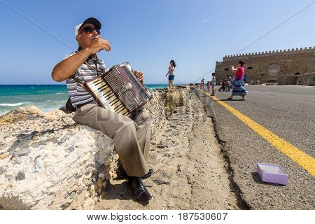 HERAKLION GREECE - JULY 16 2016: Crete. Musician on the waterfront plays accordion. In the background Venetian fortress.