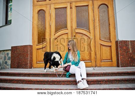 Trendy Girl At Glasses And Ripped Jeans With Russo-european Laika (husky) Dog On A Leash, Against Wo