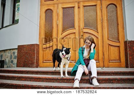 Trendy Girl At Glasses And Ripped Jeans With Russo-european Laika (husky) Dog On A Leash, Against Wo