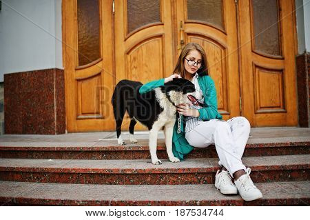 Trendy Girl At Glasses And Ripped Jeans With Russo-european Laika (husky) Dog On A Leash, Against Wo