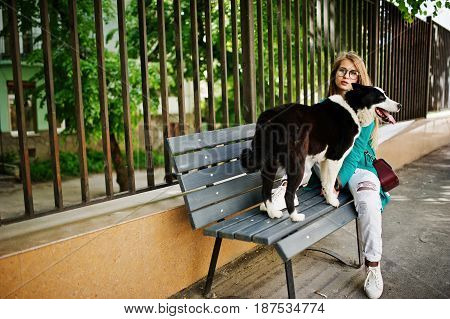 Trendy Girl At Glasses And Ripped Jeans With Russo-european Laika (husky) Dog On A Leash, Against Be