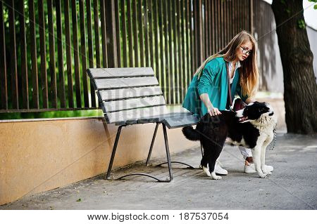 Trendy Girl At Glasses And Ripped Jeans With Russo-european Laika (husky) Dog On A Leash, Against Be