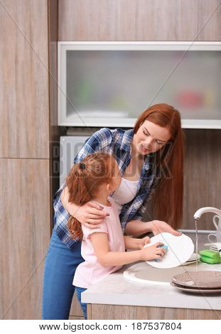 Little girl and her mother doing the washing-up in kitchen at home