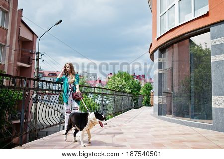 Trendy Girl At Glasses And Ripped Jeans With Russo-european Laika (husky) Dog On A Leash, Against Bu