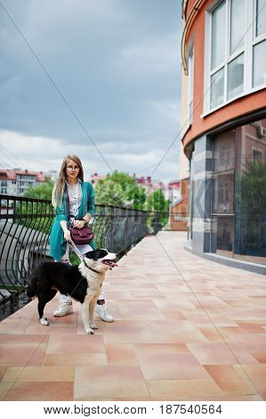 Trendy Girl At Glasses And Ripped Jeans With Russo-european Laika (husky) Dog On A Leash, Against Bu