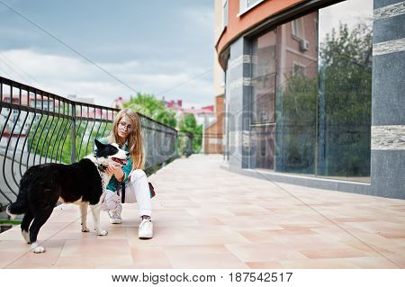 Trendy Girl At Glasses And Ripped Jeans With Russo-european Laika (husky) Dog On A Leash, Against Bu