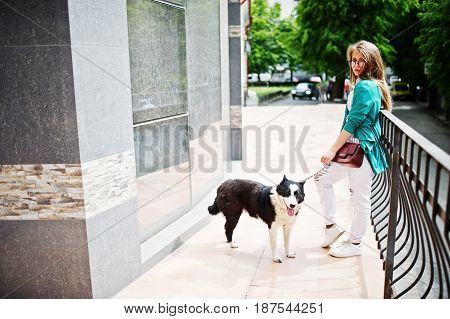 Trendy Girl At Glasses And Ripped Jeans With Russo-european Laika (husky) Dog On A Leash, Against Bu