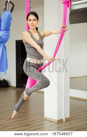 Aerial exercise or antigravity yoga indoors, meditation in sport studio or gym. Young woman making antigravity yoga exercises with pink hammock