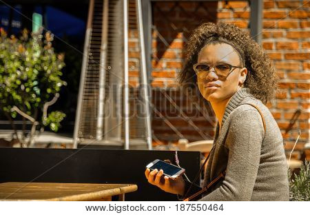 Teenage black girl with curly hair and cellphone at table at a shopping center