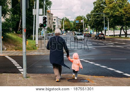 Vilnius, Lithuania  - July 5, 2016:  Elderly Woman With Little Child Girl Crossing Road At A Pedestrian Crossing In 16th Of February Street