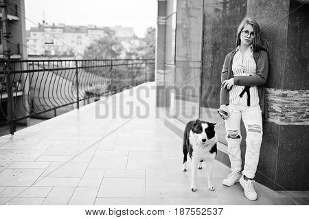 Trendy Girl At Glasses And Ripped Jeans With Russo-european Laika (husky) Dog On A Leash, Against St