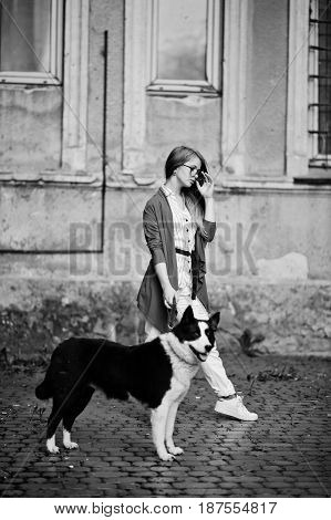 Trendy Girl At Glasses And Ripped Jeans With Russo-european Laika (husky) Dog On A Leash, Against St