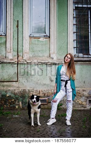 Trendy Girl At Glasses And Ripped Jeans With Russo-european Laika (husky) Dog On A Leash, Against St