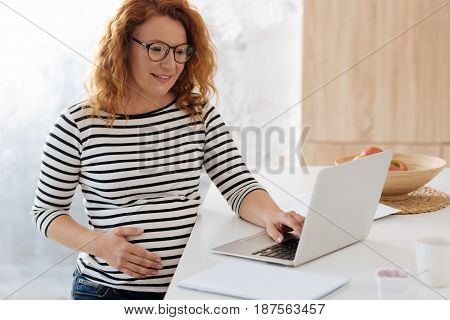 Time to work. Redhead expectant mom sitting on a bar stool and looking at a laptop while working from home.