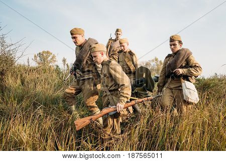 Dyatlovichi, Belarus - October 2, 2016: Reenactors Dressed As Russian Soviet Red Army Soldiers Of World War II Walking With With Maxim's Machine Gun Weapon In Autumn Meadow