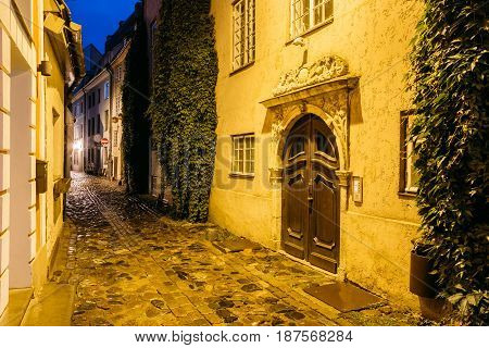 Riga, Latvia. Old Wooden Brown Door Of Portal, Decorated By Molding On Facade Of Ancient Building On Torna Street In Old Town In Lighting At Evening Or Night Illumination In Old Town. Blue Hour