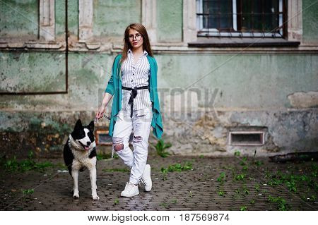 Trendy Girl At Glasses And Ripped Jeans With Russo-european Laika (husky) Dog On A Leash, Against St