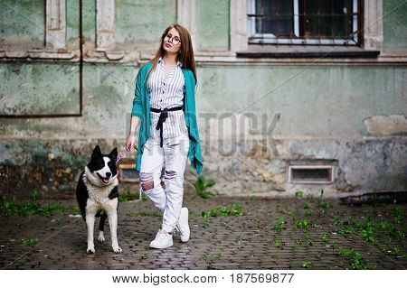 Trendy Girl At Glasses And Ripped Jeans With Russo-european Laika (husky) Dog On A Leash, Against St